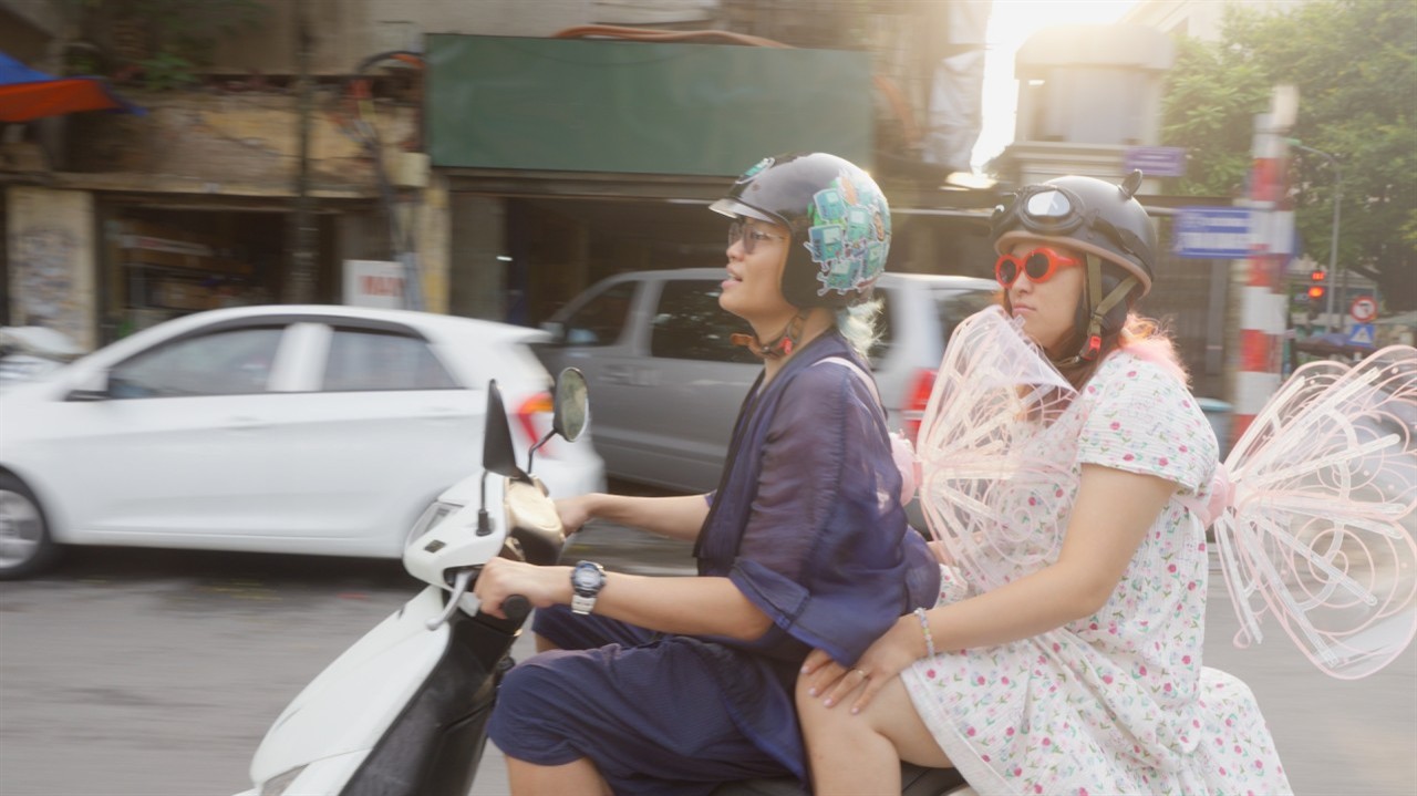 Two people wearing fairy wings on a moped